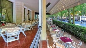 A restaurant with outdoor seating, large windows, and a view of the street. - Hotel Excelsior (Cervia)