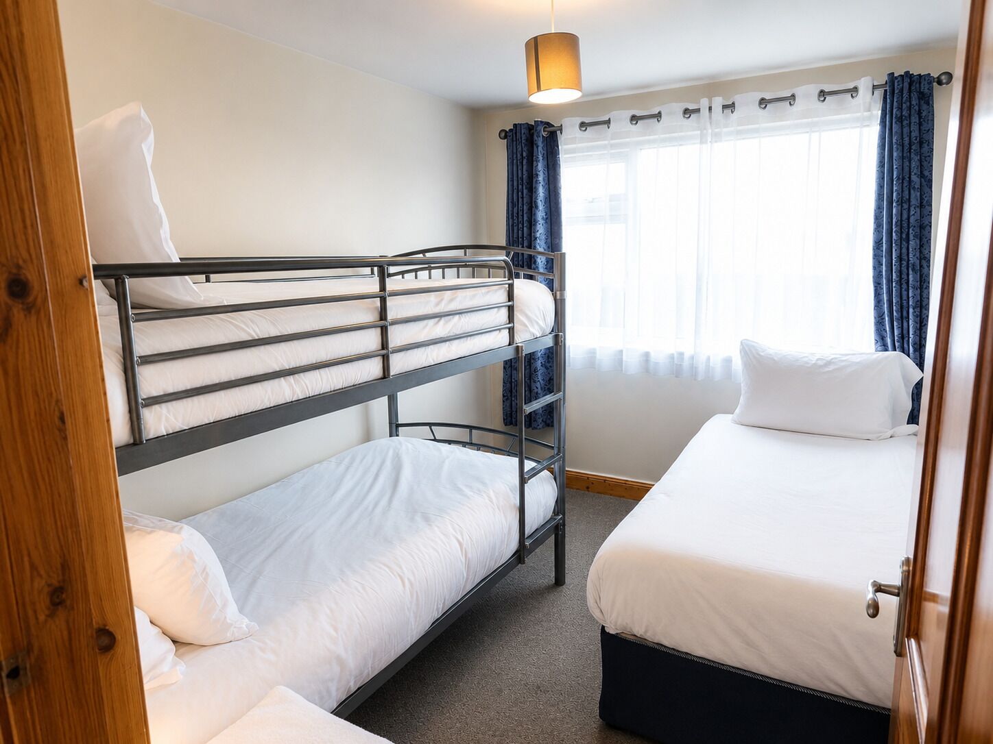 Une chambre avec un lit superposé, un lit simple, une fenêtre avec des rideaux et un luminaire suspendu.