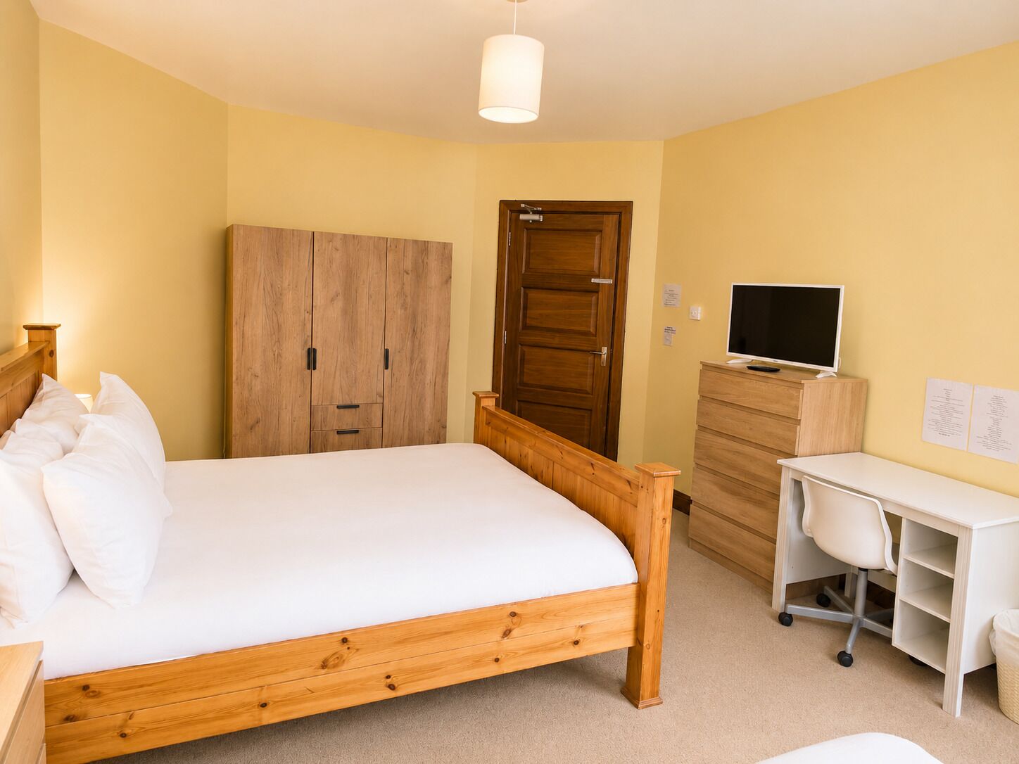 A bedroom with a wooden bed, a wardrobe, a desk with a chair, and a television.