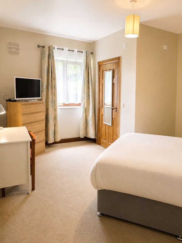 A bedroom with a bed, a desk, a television, a door, and a window with curtains. - Moorepark West House (Fermoy)