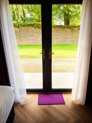 Una habitación con cama, felpudo morado y vistas a una pared de piedra y follaje.