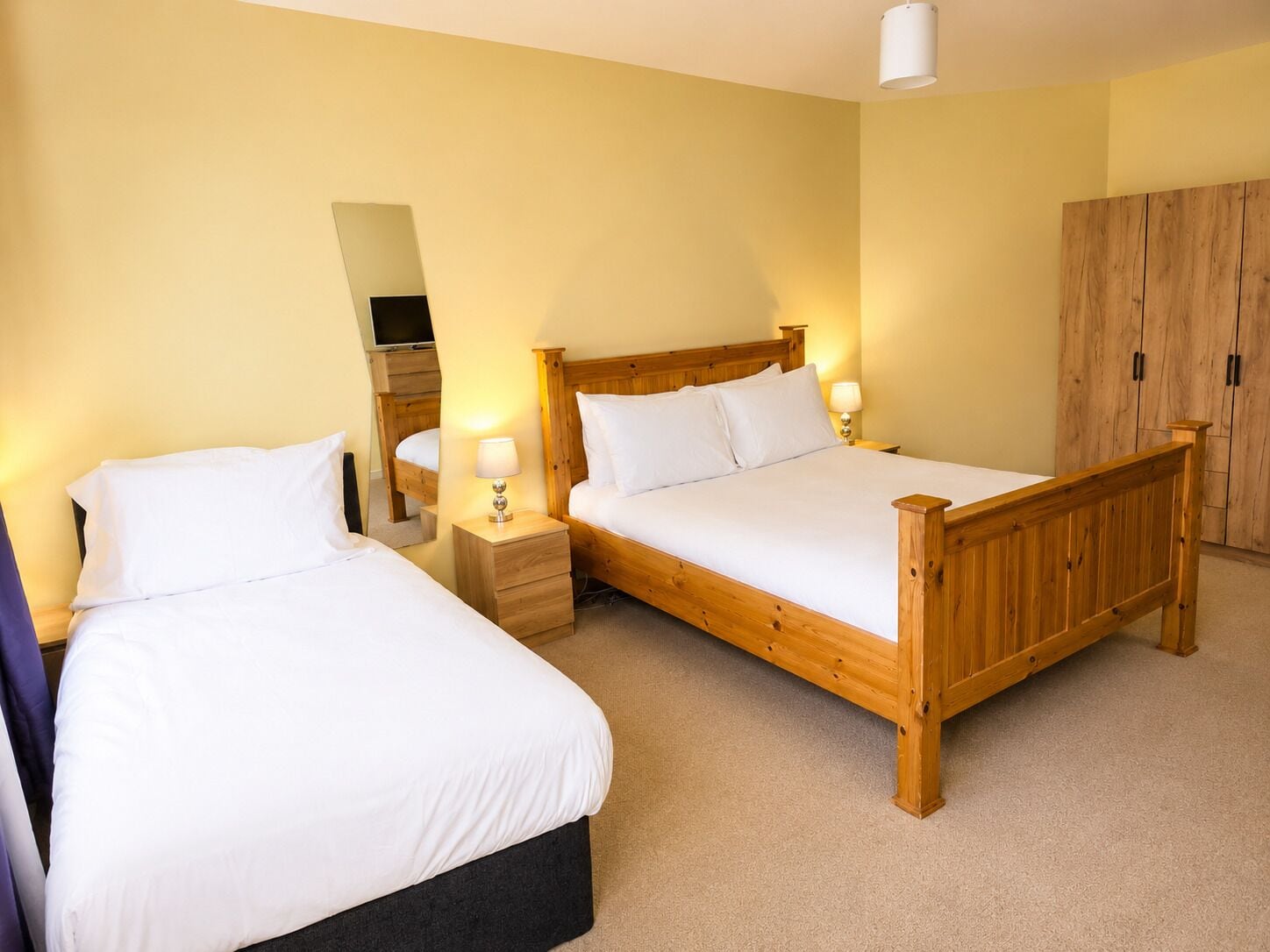 Une chambre avec deux lits en bois, un miroir, une armoire et un téléviseur.