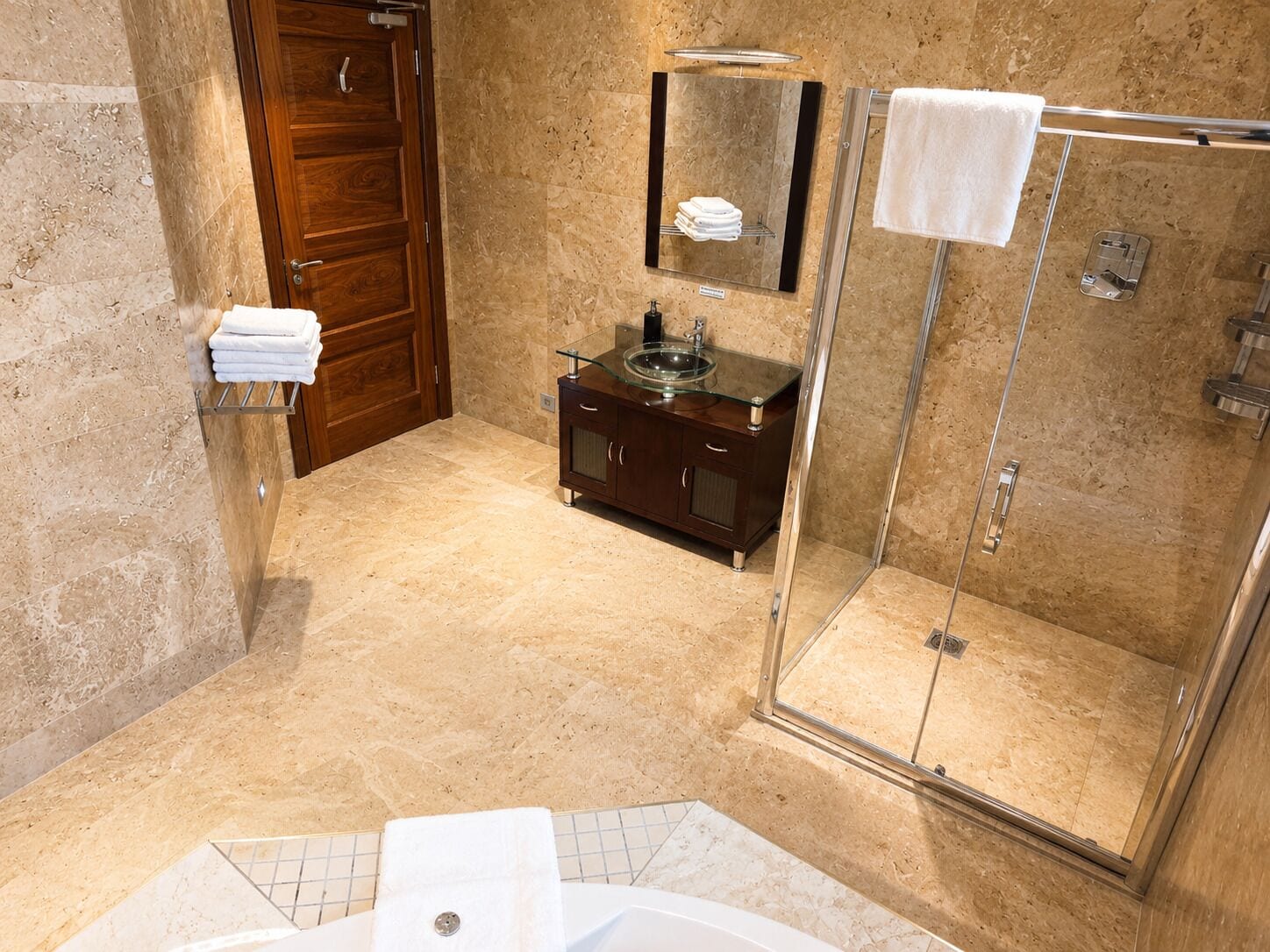 Un baño con cabina de ducha de vidrio, tocador de madera con lavamanos de cristal y suelo de baldosas de mármol.