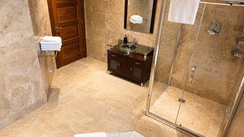 Un baño con cabina de ducha de vidrio, tocador de madera con lavamanos de cristal y suelo de baldosas de mármol.