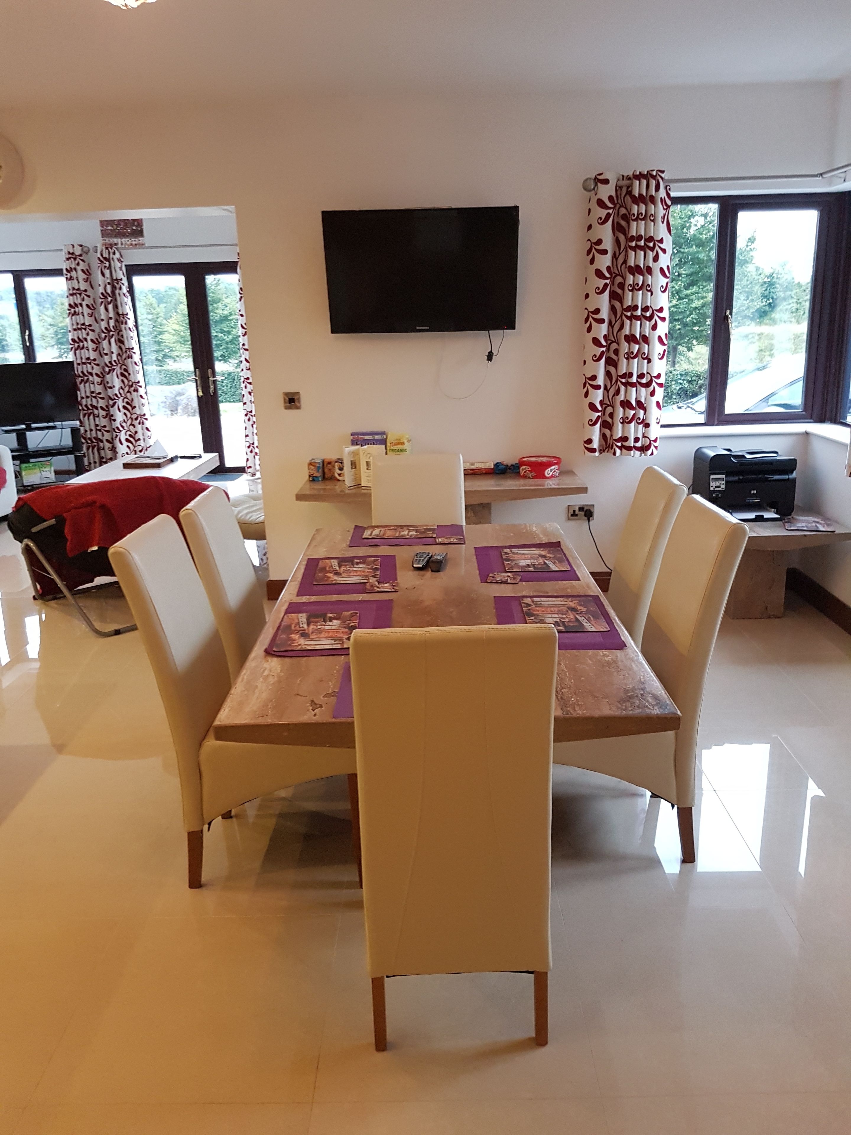 Un coin repas avec une table dressée pour six personnes, entourée de chaises. Un téléviseur à écran plat est fixé au mur au-dessus de la table.
