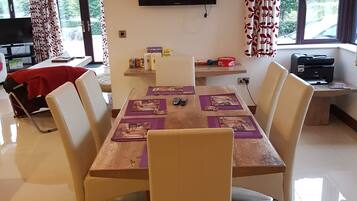 Un coin repas avec une table dressée pour six personnes, entourée de chaises. Un téléviseur à écran plat est fixé au mur au-dessus de la table.