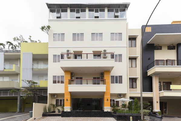 Un edificio de varios pisos con entrada central, balcones y unidades de aire acondicionado.