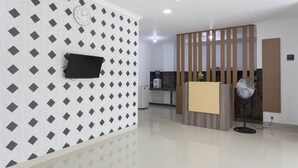 A modern reception area with a patterned wall, a clock, a flat-screen TV, a fan, and a wooden partition. - RedDoorz Plus @ Boulevard Residence BSD (South Tangerang)