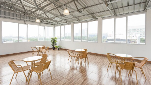 A spacious room with large windows, wooden flooring, and multiple round tables with wicker chairs. - RedDoorz Plus @ Boulevard Residence BSD (South Tangerang)