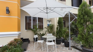 A patio with a white umbrella, white chairs, and potted plants. - RedDoorz Plus @ Boulevard Residence BSD (South Tangerang)