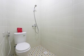 Un baño pequeño con azulejos, que incluye un inodoro, una ducha y un estuche rojo de pañuelos sobre el inodoro.