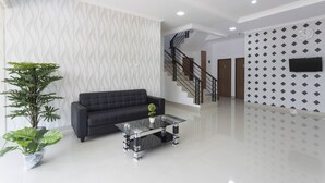 A modern living room with a black sofa, a glass coffee table, and potted plants. - RedDoorz Plus @ Boulevard Residence BSD (South Tangerang)