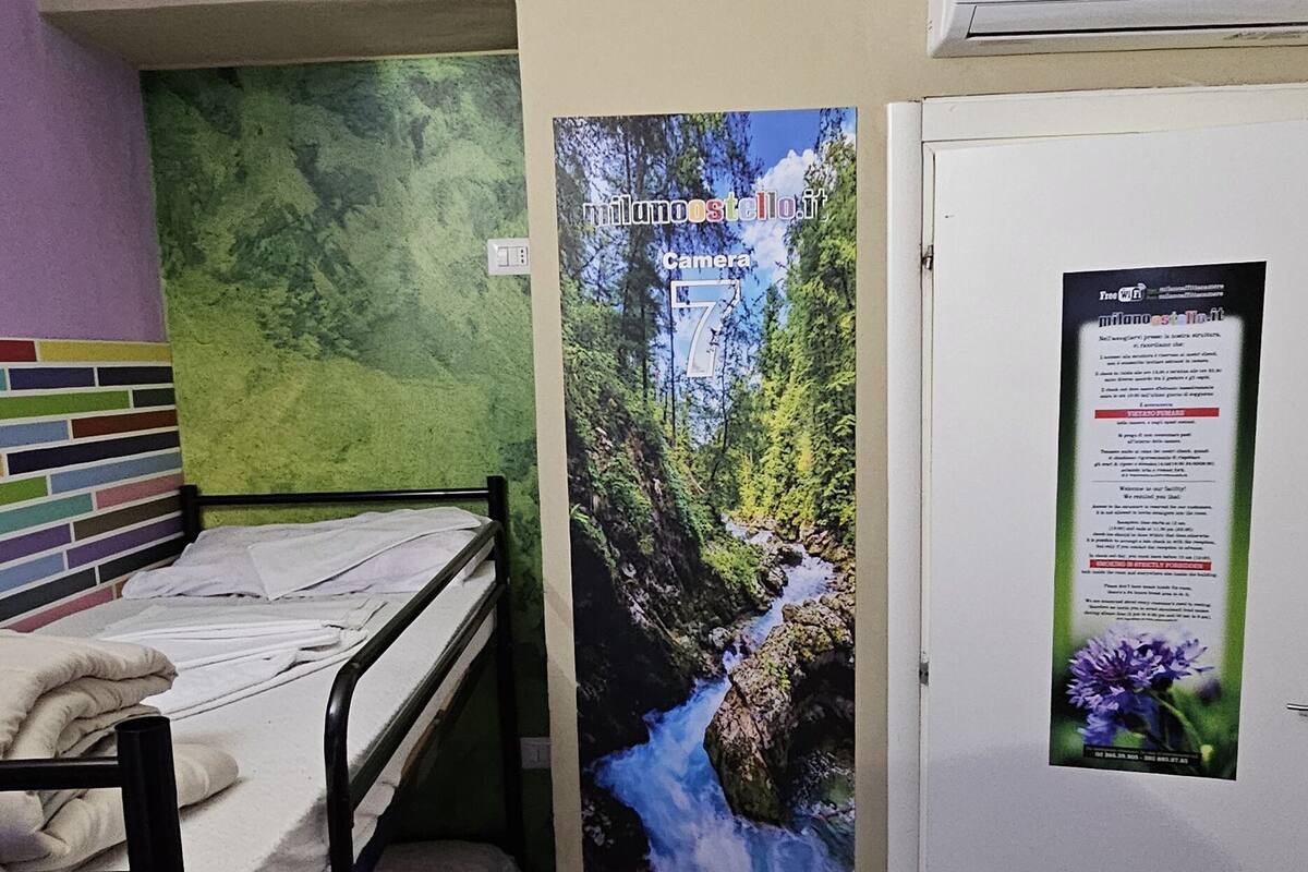A small room with a bunk bed, a green textured wall, a poster of a waterfall, and a door with a bulletin board.