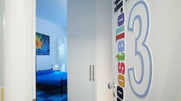 Een hotelkamer met een bed, een deur met een kleurrijk bord en een blauw geruit vloertje.