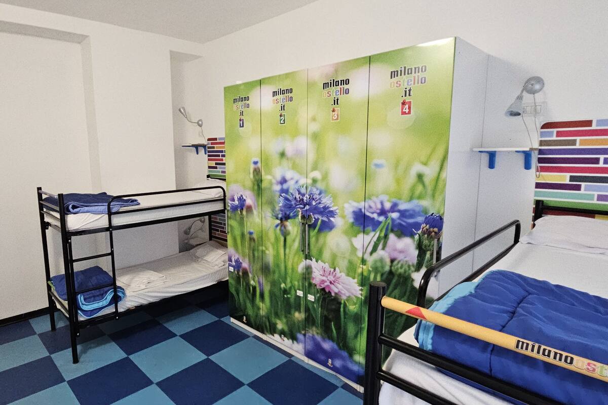 A dormitory room with bunk beds, a green wall with a floral mural, and a colorful brick-patterned wall.