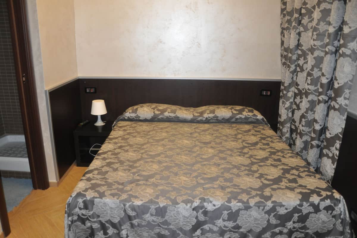 A bedroom with a bed, a nightstand, a lamp, and a shower area.