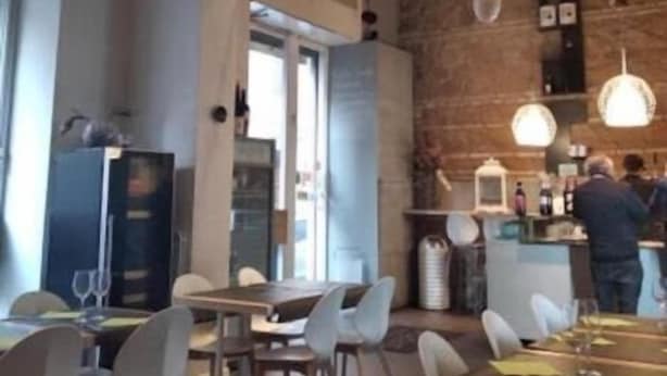 A restaurant interior with high ceilings, exposed brick walls, and hanging pendant lights. Tables are set with chairs, and a bar area is visible in the background. - Funny Palace Hostel (Rome)