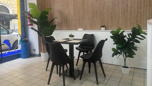 A dining area with a wooden slat wall, a tiled floor, and black chairs around a small table. - Funny Palace Hostel (Rome)