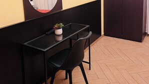 A room with a wooden herringbone floor, a black desk with a chair, a round mirror, a television mounted on the wall, and a wardrobe. - Funny Palace Hostel (Rome)