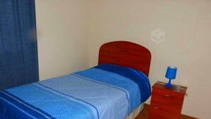 A single bed with a blue and white bedspread, a wooden headboard, and a small bedside table with a blue lamp. - Laguna del Mar (La Serena)