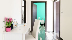 A modern hotel room with a white desk, a potted plant, and a teal-colored wall.