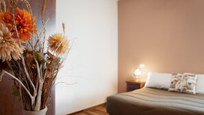 A bedroom with a bed, a bedside table with a lamp, and a vase with dried flowers.