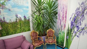 A room with a purple sofa, two ornate chairs, a large potted plant, and floral wall art. - Milano Affittacamere (Milan)