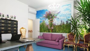A modern living room with a purple sofa, a desk with a laptop, a chandelier, and a large floral mural on the wall. - Milano Affittacamere (Milan)