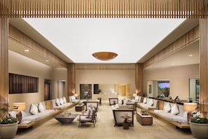 A spacious hotel lobby with a high ceiling, wooden paneling, and a central light fixture. There are multiple seating areas with sofas and armchairs, and a reception desk in the background. - Ventus at Marina El Cid Spa & Beach Resort - All Inclusive (Puerto Morelos)