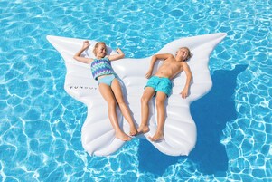 Two children lying on a white inflatable float in a swimming pool.