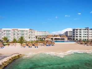 A resort with multiple hotel buildings, a swimming pool, beach area with lounge chairs, and a rocky shoreline. - Ventus at Marina El Cid Spa & Beach Resort - All Inclusive (Puerto Morelos)
