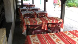 Een restaurant met tafels, gedekt met rode en beige tafelkleden met een patroon, gerangschikt in rijen met stoelen.