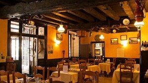 Een restaurant met houten balken, tafels met gele tafelkleden en hangende lampen.