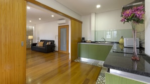 Una cocina moderna con armarios verdes, suelo de madera y una zona de comedor con sofá y lámpara.