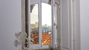 Una habitación con ventana que da a un paisaje urbano, incluyendo una cúpula y tejados de tejas.