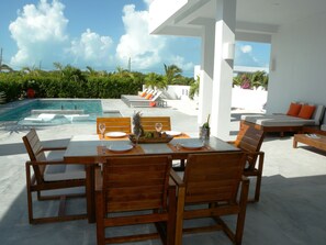 A poolside dining area with a table set for two, a lounge chair, and a sofa.