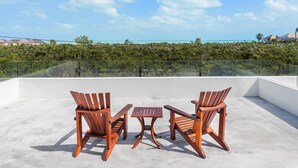 A rooftop terrace with three wooden chairs and a small table, overlooking a lush landscape and a clear blue sky. - White Villas (Providenciales)