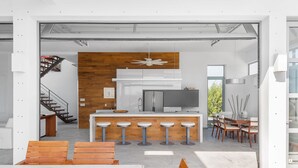 A modern kitchen with a wooden accent wall, a central island with bar stools, and a dining area with wooden chairs and a table. - White Villas (Providenciales)