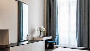 Ein modernes Hotelzimmer mit Bett, Schreibtisch mit Stuhl, einem großen Spiegel und einem Fenster mit Vorhängen.