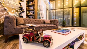 Eine moderne Lobby mit einem gepolsterten braunen Sofa, einem weißen Couchtisch mit einem Vintage-Spielzeuglkw und einem Bücherregal voller Bücher.
