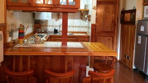 Una cocina con gabinetes de madera, una isla central con taburetes, un lavaplatos y un refrigerador.