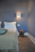 Un dormitorio con cama, almohadas, una mesita de noche con lámpara y un enchufe en la pared.