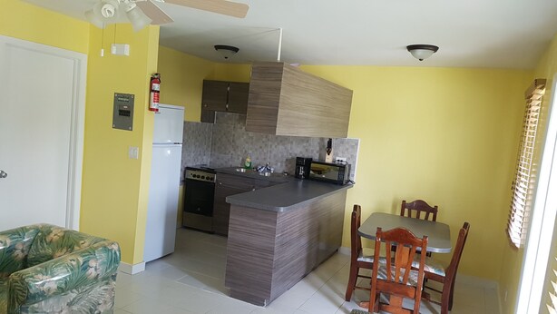 A compact kitchen with a central island, a dining area with a table and chairs, and a ceiling fan. - The Tranquil  C's (Nassau)