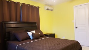 A bedroom with a bed, brown curtains, a white door, and an air conditioning unit. - The Tranquil  C's (Nassau)