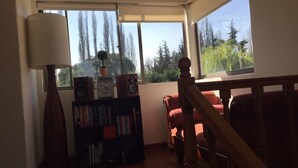 Una habitación con estantería, lámpara, silla y ventana con vistas a árboles.