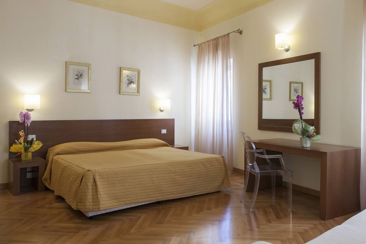 Une chambre d’hôtel avec un grand lit, un bureau, une chaise et deux lampes fixées au mur.