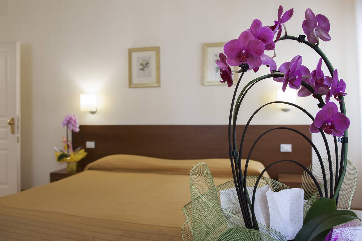 Une chambre d’hôtel avec un lit soigneusement fait, une composition florale décorative à base d’orchidées et deux tableaux encadrés accrochés au mur.