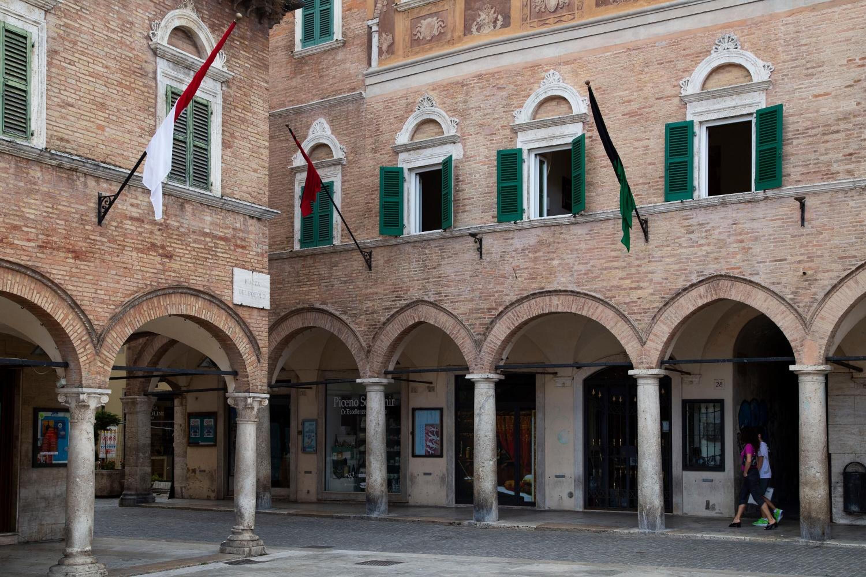 Un patio con paseos arqueados y fachada de edificio con contraventanas verdes.