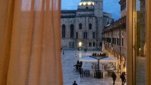 Une cour ouverte, avec un bâtiment historique doté d’un dôme et d’un clocher, entourée de murs de pierre et où quelques personnes se promènent.