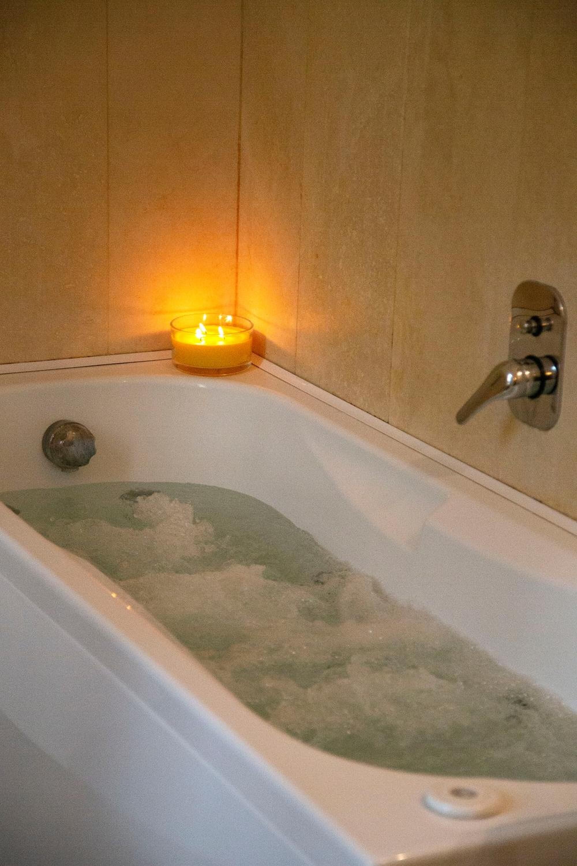 Una bañera con una vela encendida, un grifo y una pared con azulejos.